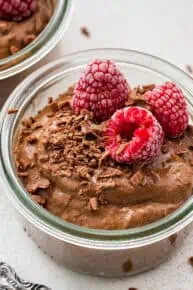 Close up of a jar of chocolate avocado mousse topped with raspberries