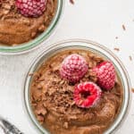 Overhead view of a jar of chocolate avocado mousse, topped with raspberries, next to another jar of it