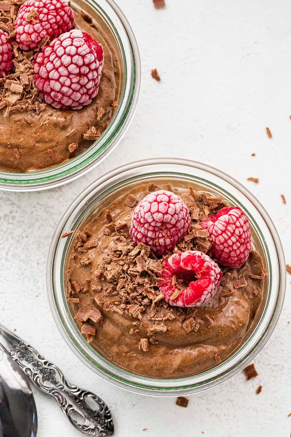 Overhead view of a jar of chocolate avocado mousse, topped with raspberries, next to another jar of it