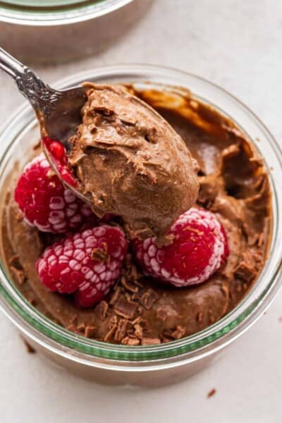 A spoon pulling out a bite of chocolate avocado mousse from a bowl of mousse topped with raspberries