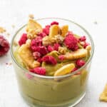 A jar of banana avocado mousse topped with banana chips and raspberries