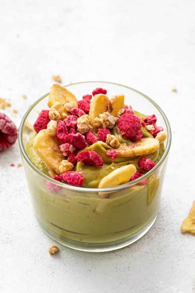 A jar of banana avocado mousse topped with banana chips and raspberries