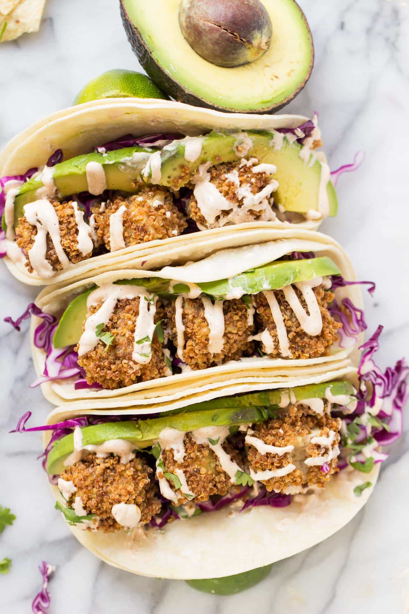 Three crispy tofu tacos with red cabbage, avocado, and a crema, next to half an avocado