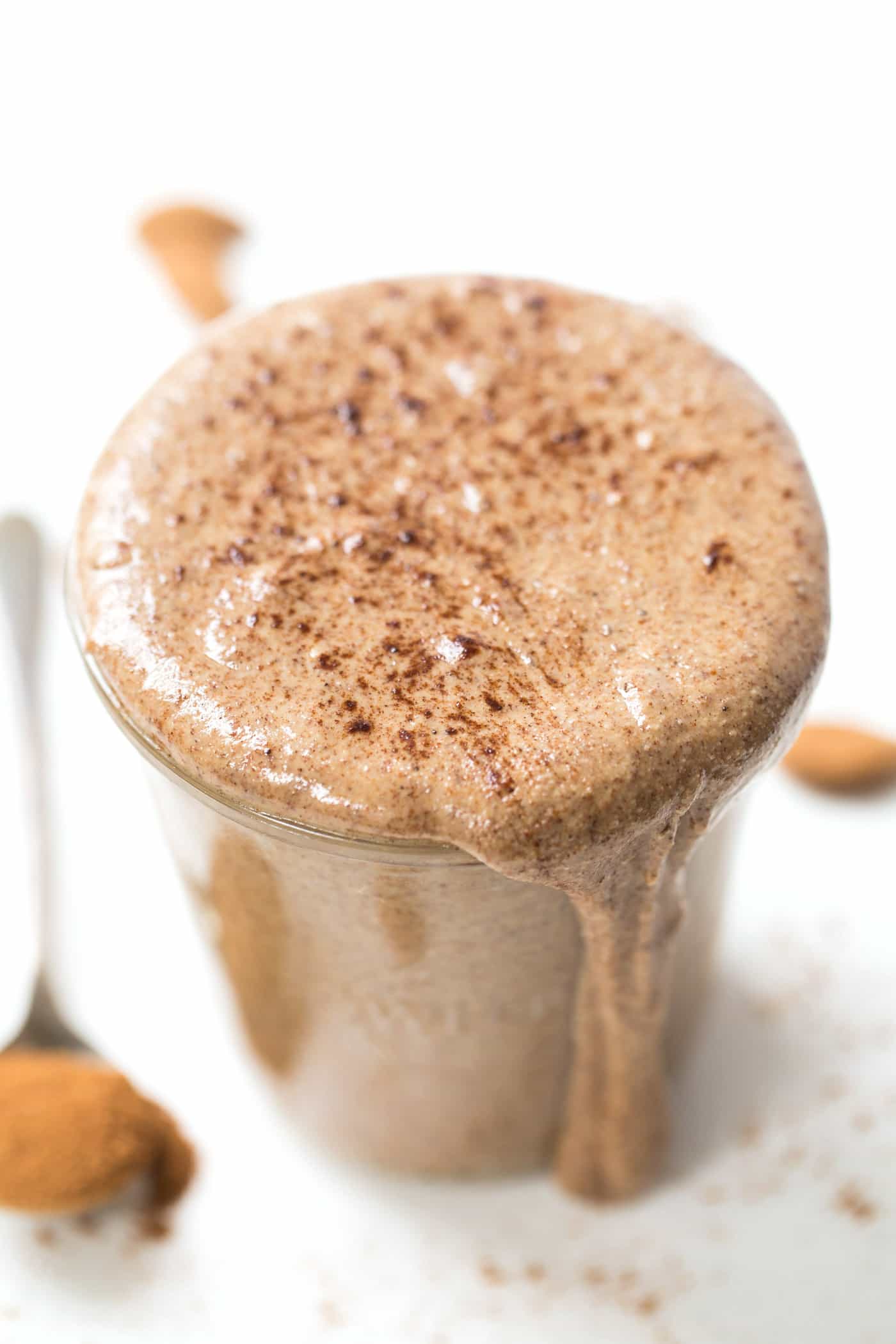 A jar of homemade nutella with cocoa powder on top, dripping down the jar, with a spoon of cocoa powder in the background