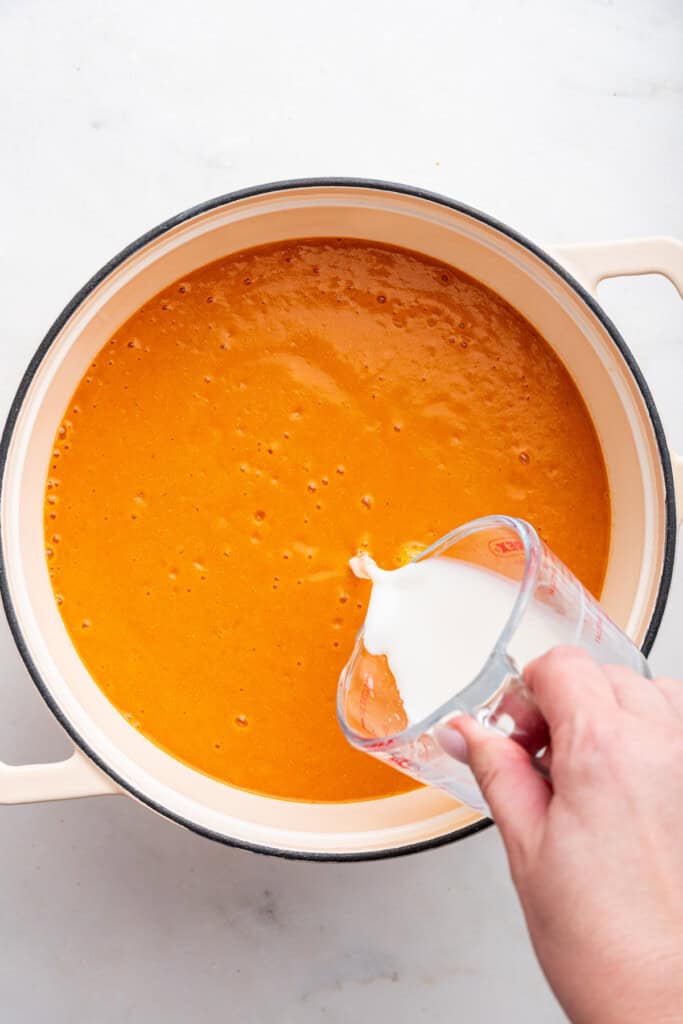 Adding almond milk to blended tomato bisque soup.