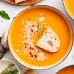 Tomato bisque in a bowl with a piece of toast on top.