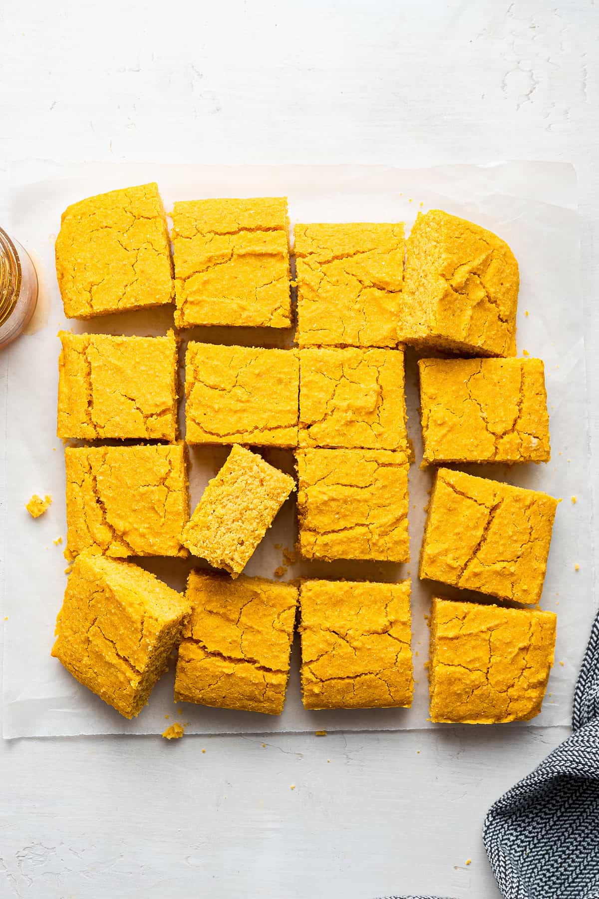 This vegan pumpkin cornbread recipe is moist, tender, and full of fall flavors, plus it's gluten-free and only uses one bowl. Overhead view of vegan pumpkin cornbread, cut into squares, all separated slightly