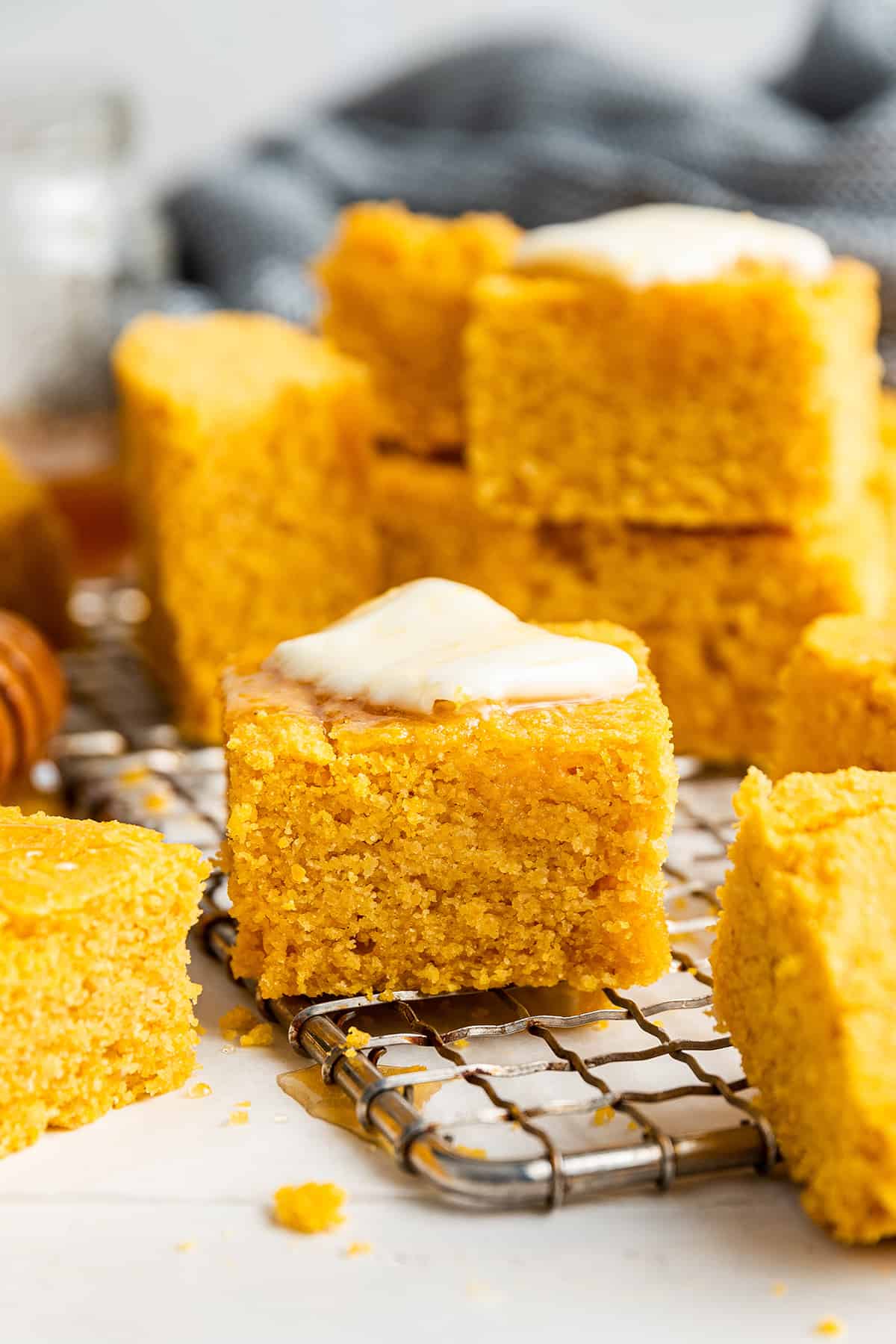 This vegan pumpkin cornbread recipe is moist, tender, and full of fall flavors, plus it's gluten-free and only uses one bowl. Close up of a slice of vegan pumpkin cornbread with a pat of butter on top, on a wire rack, with other slices surrounding it