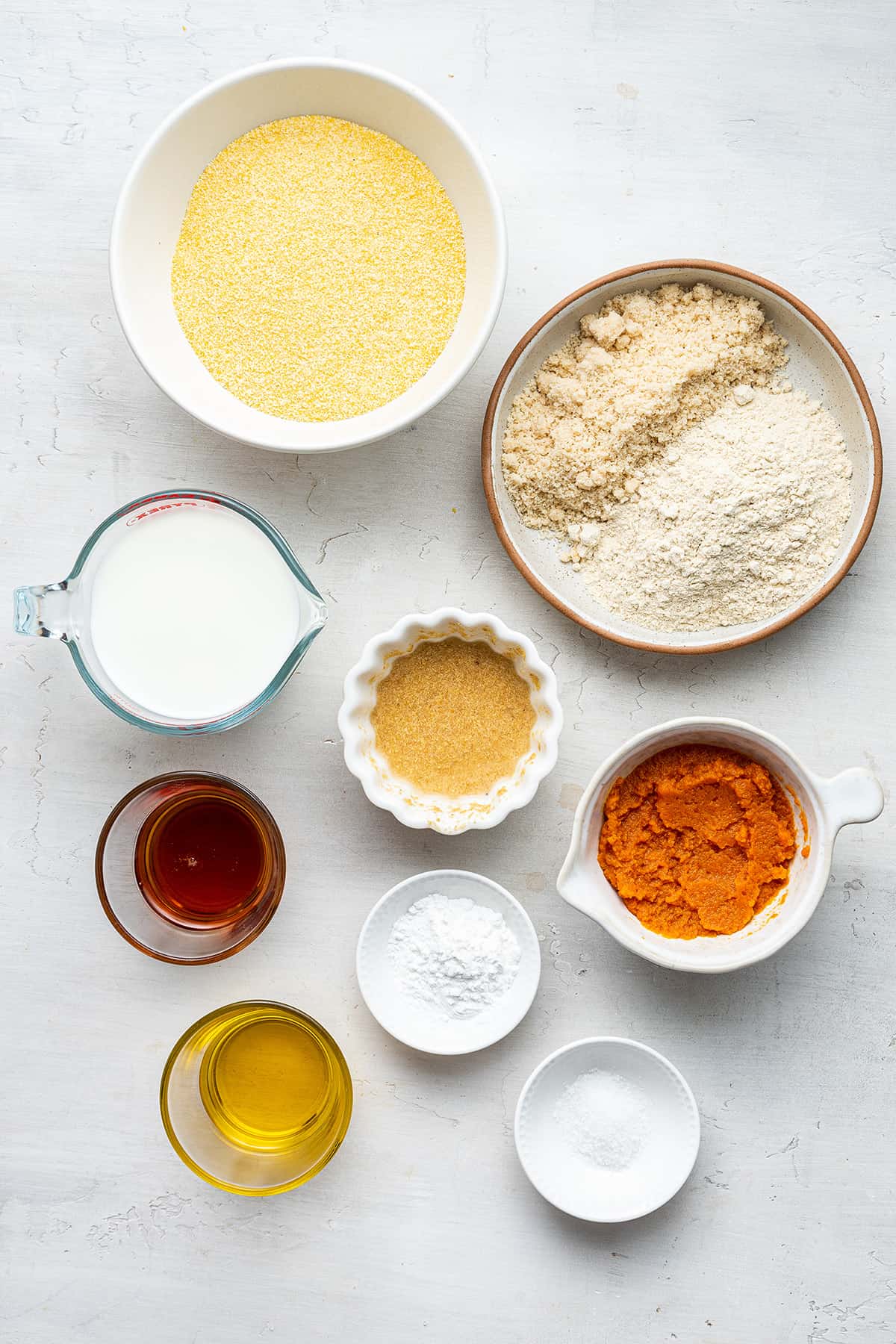 This vegan pumpkin cornbread recipe is moist, tender, and full of fall flavors, plus it's gluten-free and only uses one bowl. Overhead view of the ingredients for vegan pumpkin cornbread: cornmeal, almond flour, quinoa flour, pumpkin puree, a flax bomb, almond milk, salt, olive oil, maple syrup, and baking powder