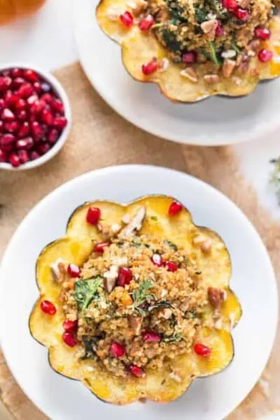 Overhead view of two mushroom and quinoa stuffed acorn squash on plates, topped with pomegranate seeds.