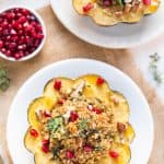 Overhead view of two mushroom and quinoa stuffed acorn squash on plates, topped with pomegranate seeds.