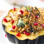 Mushroom and quinoa stuffed acorn squash on a white plate topped with pomegranate seeds.