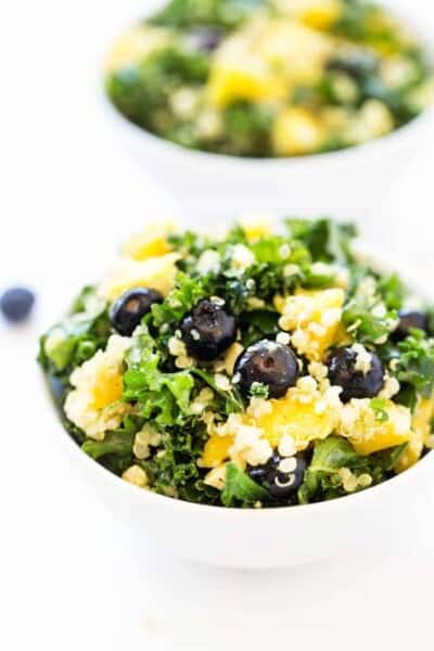 A bowl of refreshing kale and quinoa salad with lemon dressing and sweet blueberries.