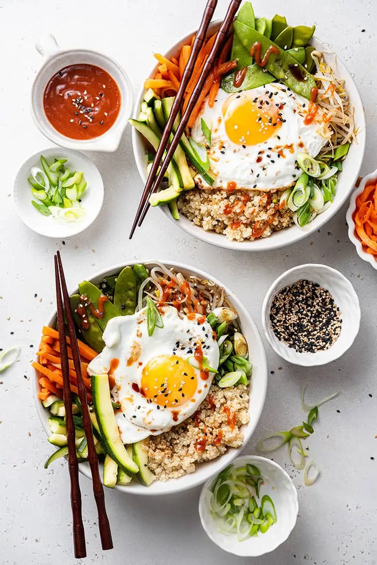 Two bowls of quinoa bibimbap with steamed veggies and sunny side up egg