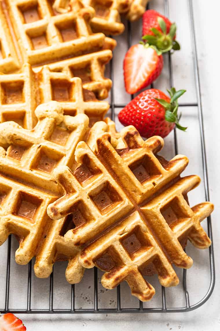 Three waffles on a cooling rack with sliced strawberries