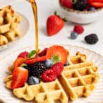 Pouring maple syrup on an almond flour waffle with berries