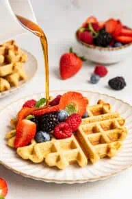 Pouring maple syrup on an almond flour waffle with berries