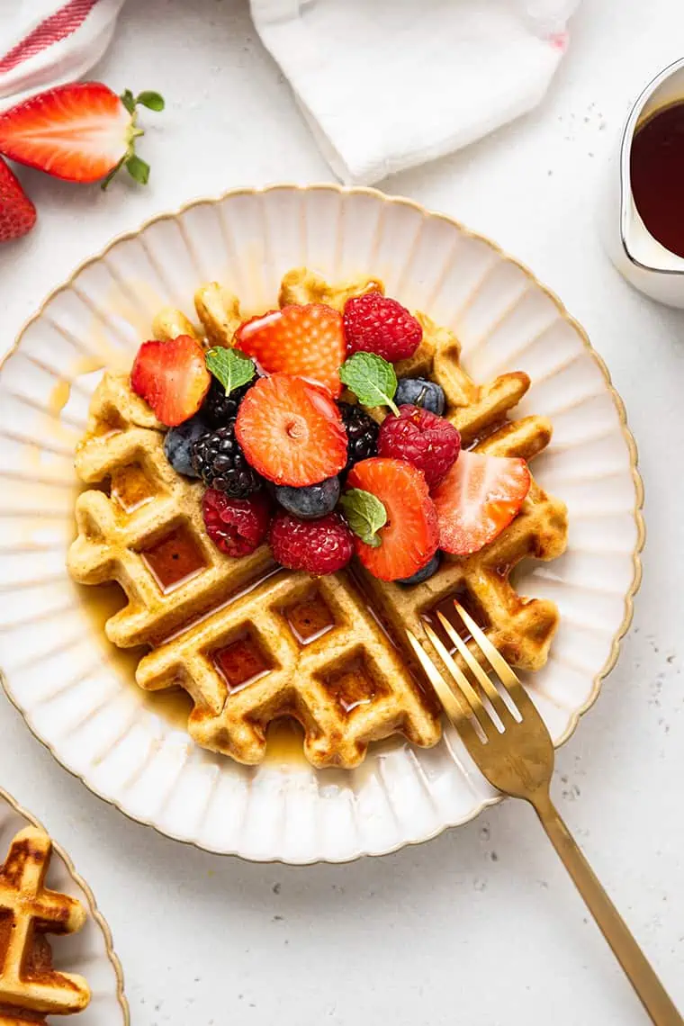 A waffle on a plate with berries and a fork