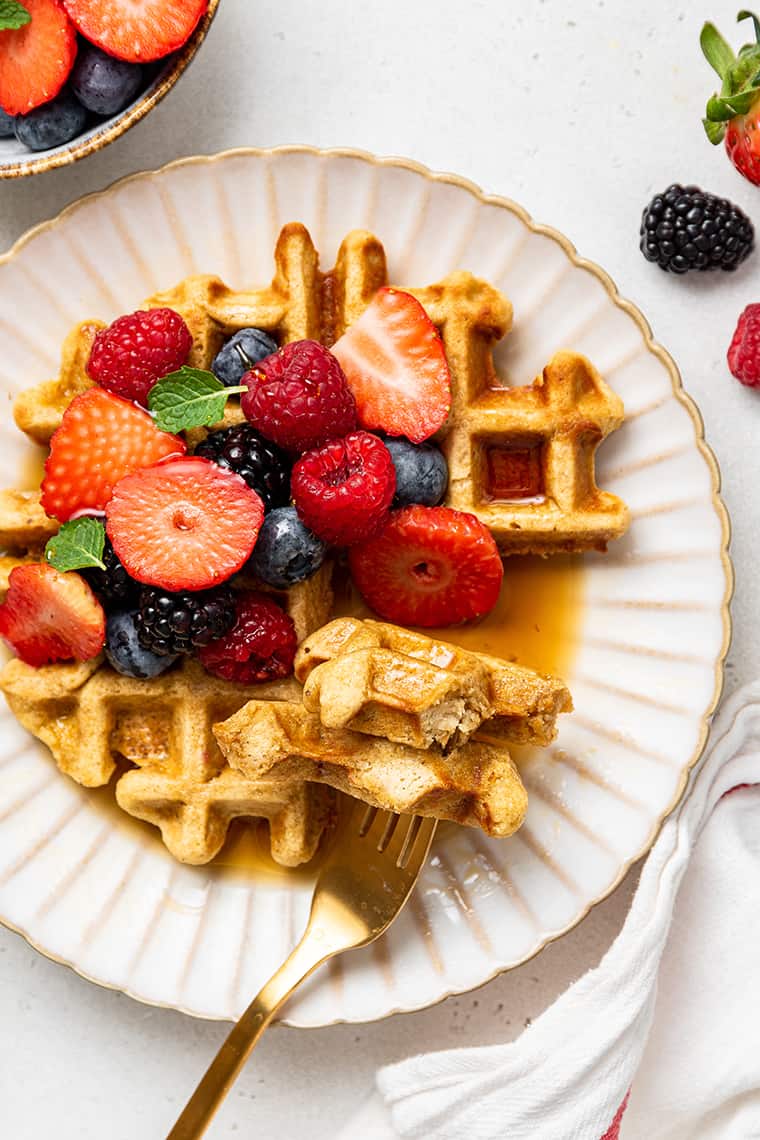 Top view of almond flour waffles, a bite full on a fork, with berries.