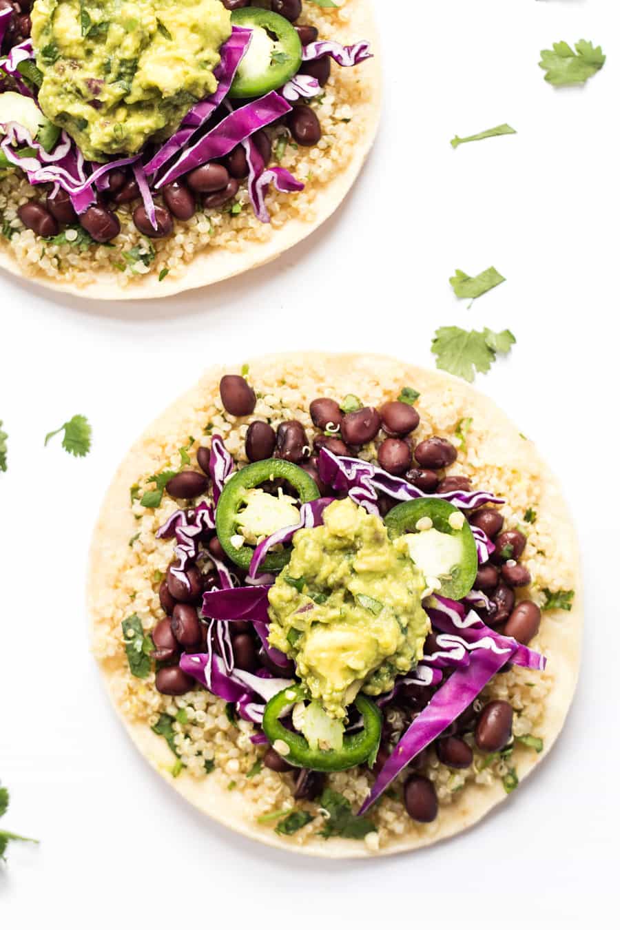 overhead of two tortillas with black beans, quinoa, guacamole, jalapenos and cabbage