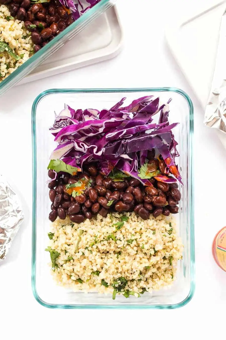 overhead of a glass meal prep container with the ingredients for cilantro lime tacos with quinoa, cabbage and black beans