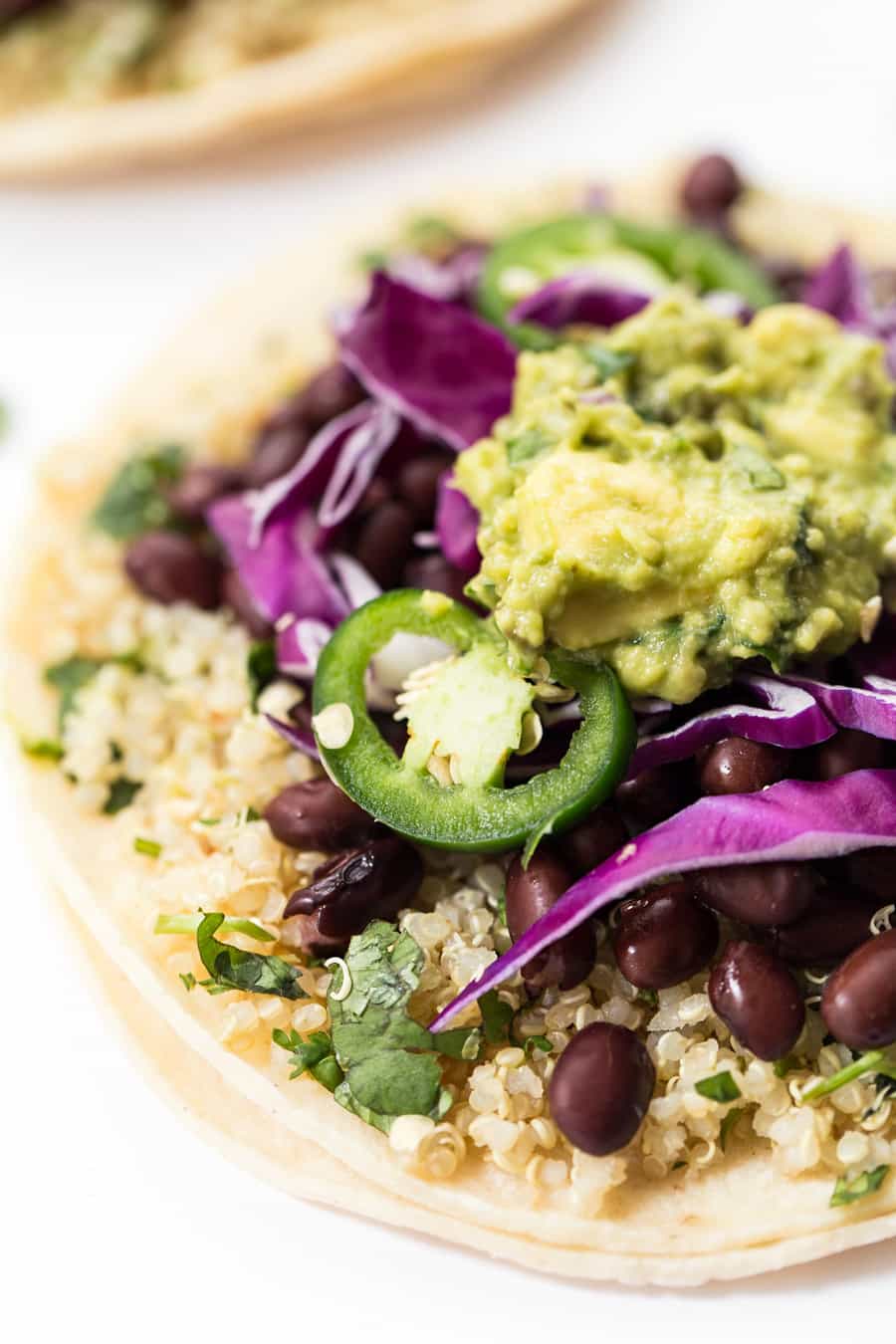 Close up on a tortilla topped with quinoa, black beans, guacamole, cabbage and peppers