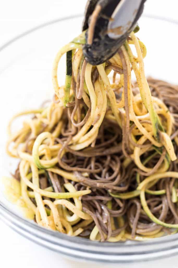 Tossing zoodles and soba noodles with sauce in bowl