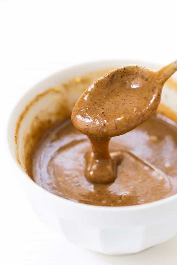 creamy almond butter sauce dripping off of spoon into bowl