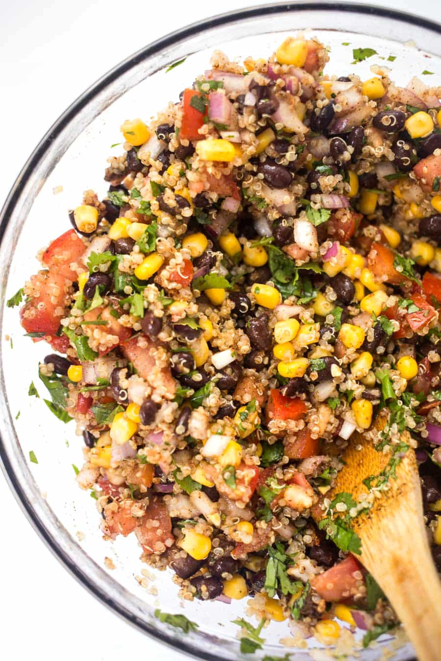 Corn, black beans, tomatoes, herbs and onions in a clear bowl. They are the ingredients for Mexican Quinoa Stuffed Peppers. 