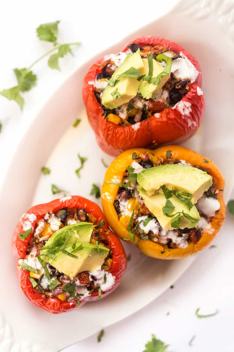 MEXICAN Quinoa Stuffed Peppers rest on a white plate. They are covered in avocado and herbs. 