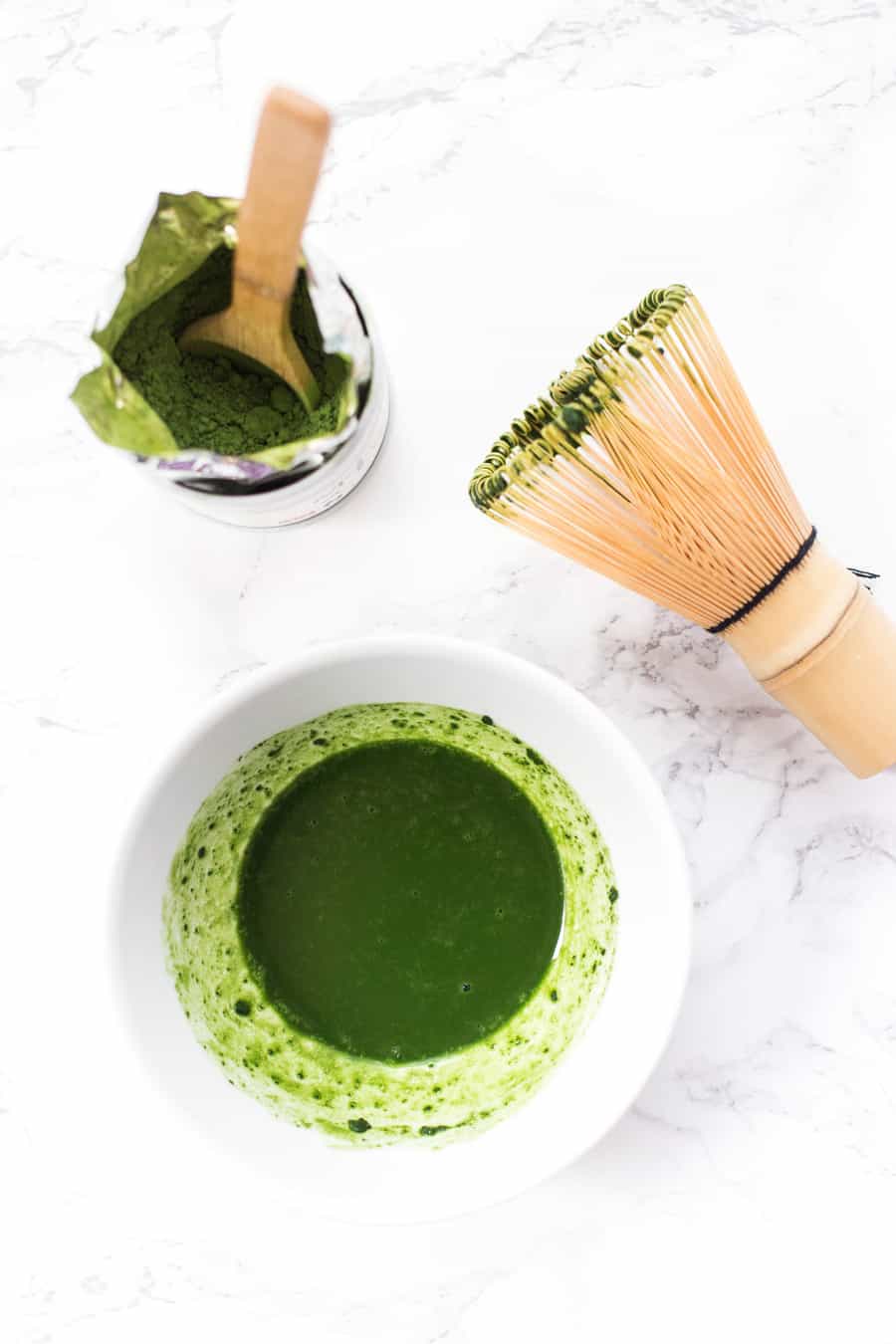 Overhead view of matcha powder, whisk, and matcha in small bowl
