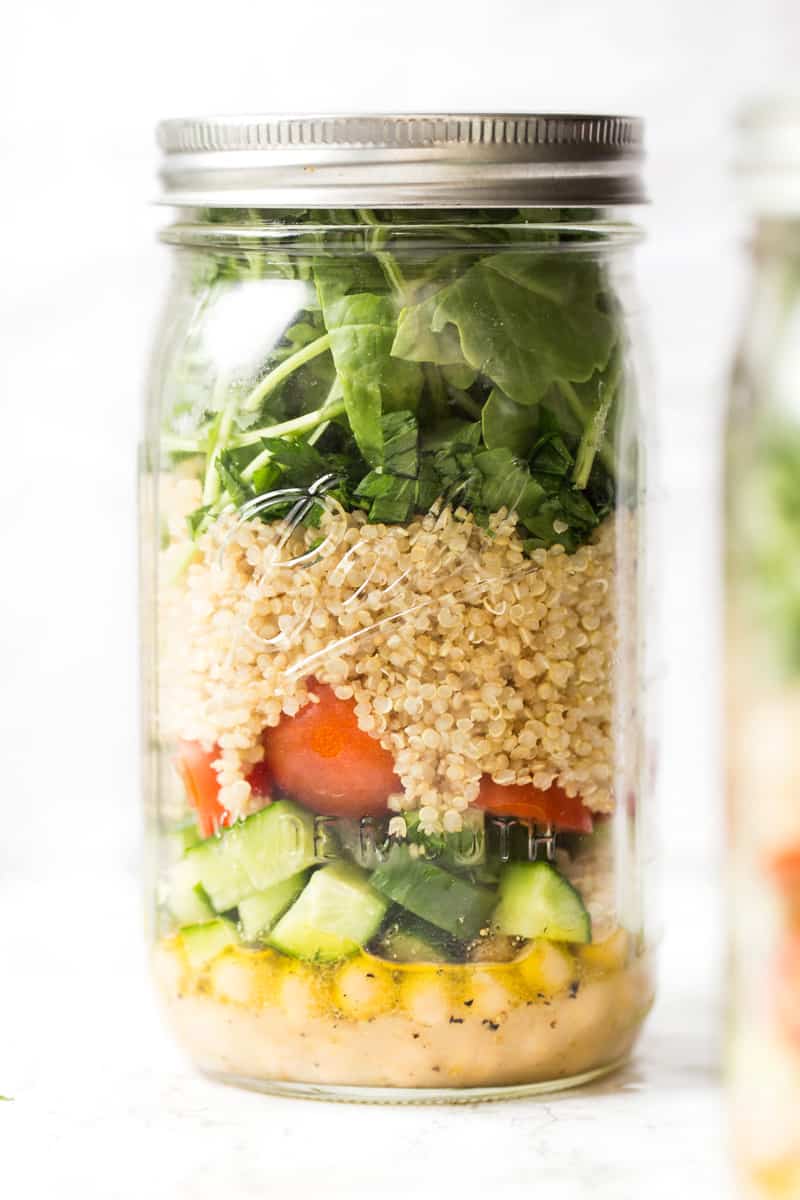 A mason jar with the lid on top. It is filled with salad greens, quinoa, vegetables, chickpeas and salad dressing. 