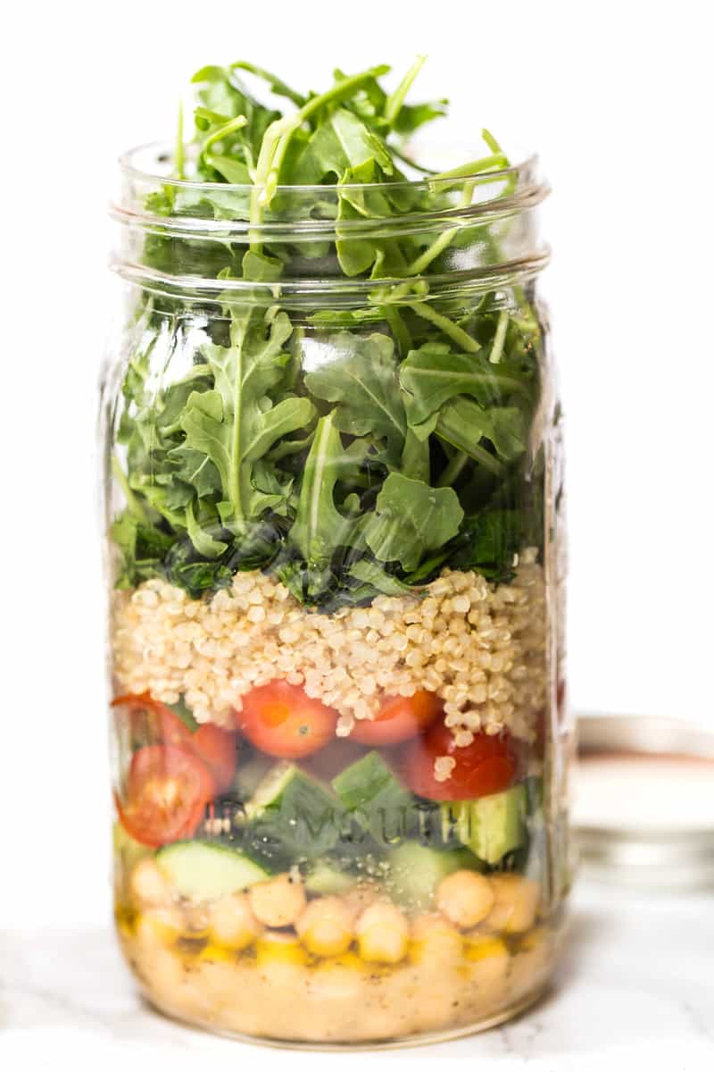A mason jar filled with salad greens, quinoa, vegetables, chickpeas and dressings.