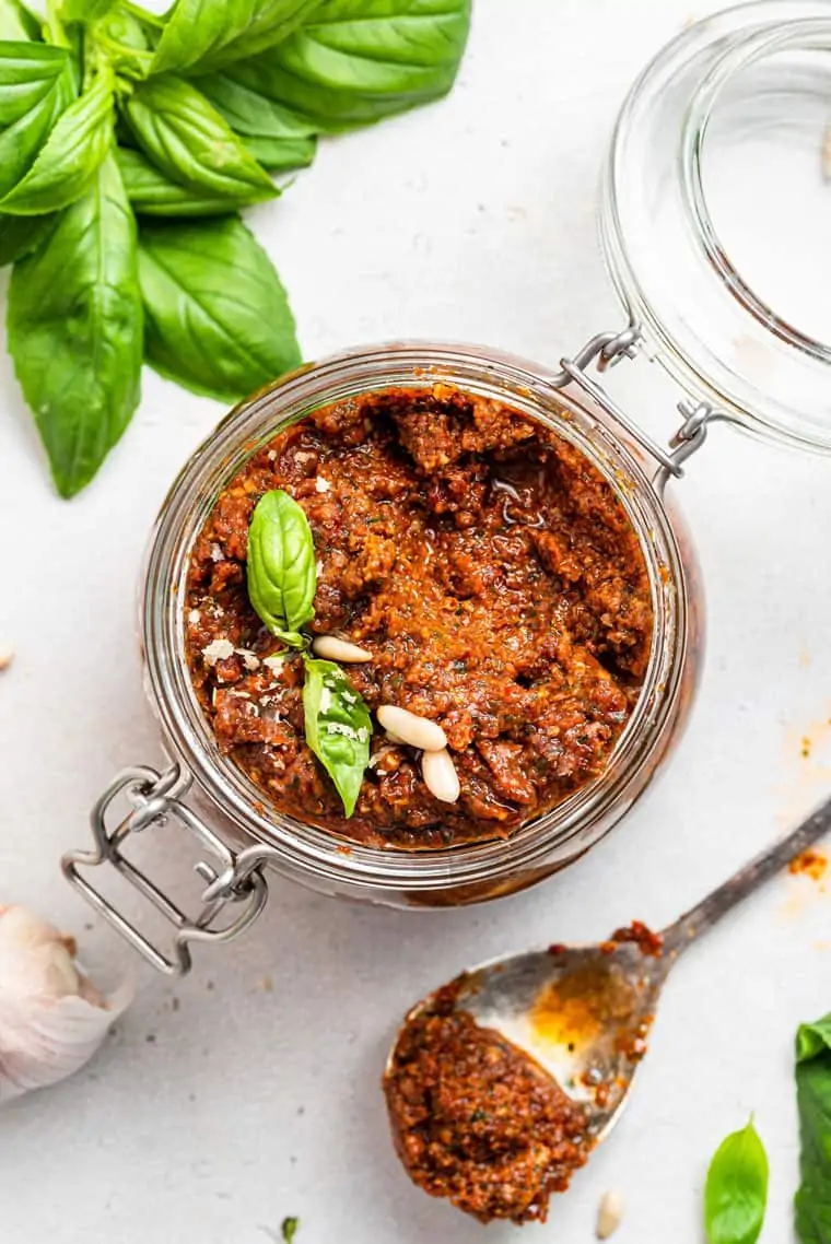 glass jar of sun dried tomato pesto with nuts and basil