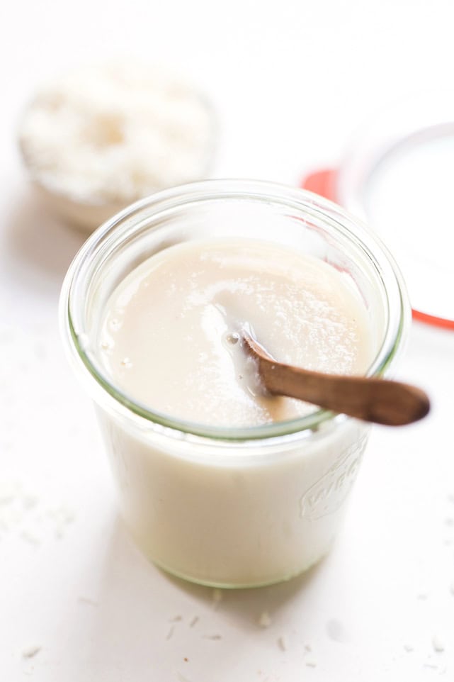 A glass jar of coconut butter, with a wooden spoon resting in it