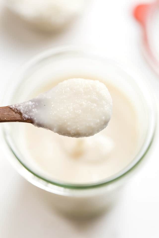 A wooden spoon lifting a spoonful of coconut butter out of a jar