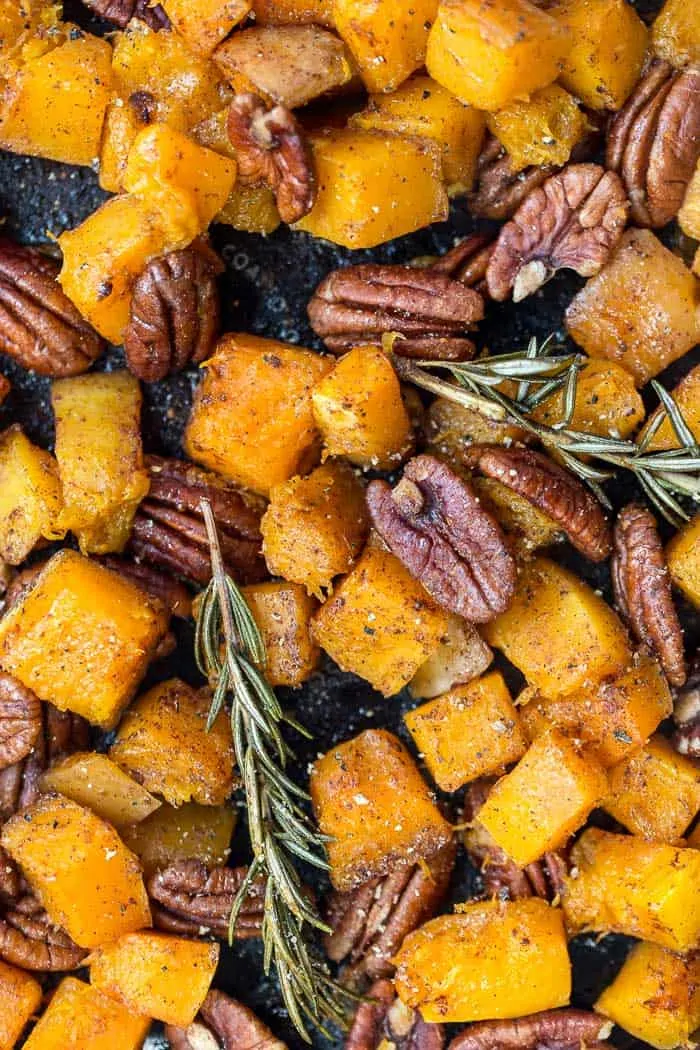 Overhead view of roasted butternut squash on pan with rosemary sprigs and pecan halves