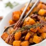 Cinnamon maple roasted butternut squash in serving dish with rosemary and pecans