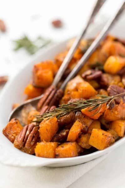 Cinnamon maple roasted butternut squash in serving dish with rosemary and pecans