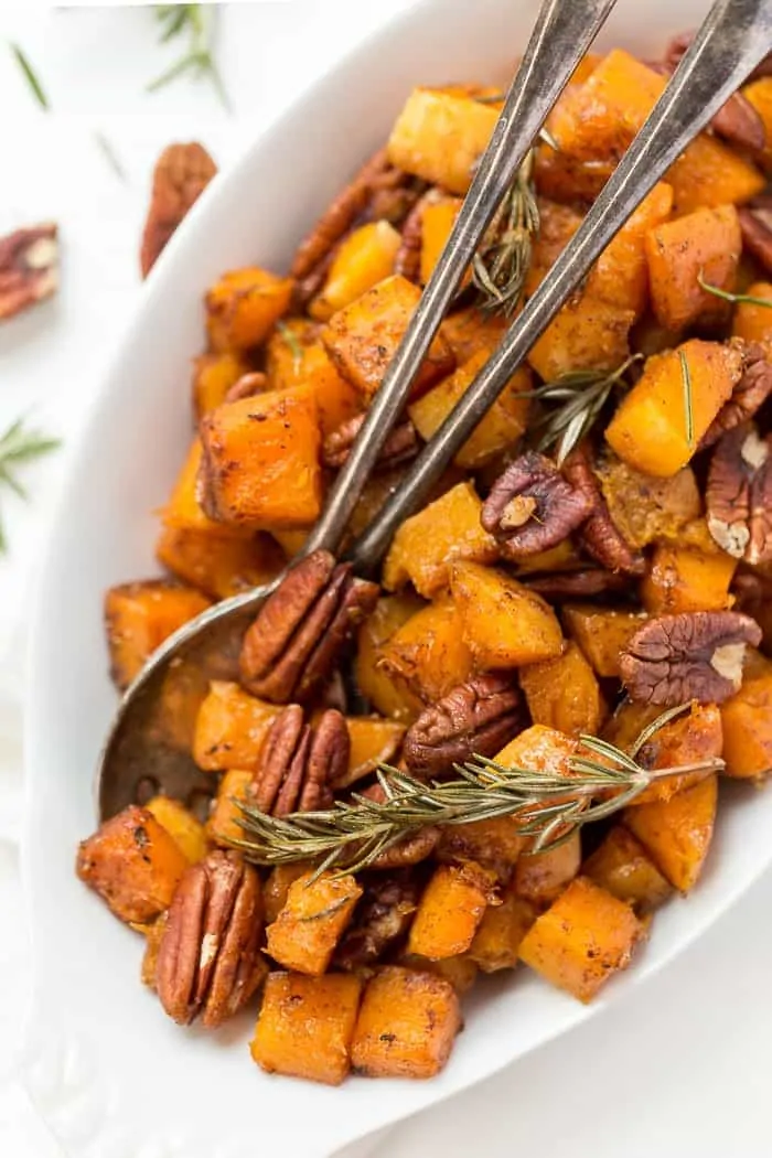With tender squash, toasty pecans and maple glaze, this roasted butternut squash is a perfect holiday side, but easy enough for a weeknight! Overhead view of maple roasted butternut squash in serving dish with pecans and rosemary