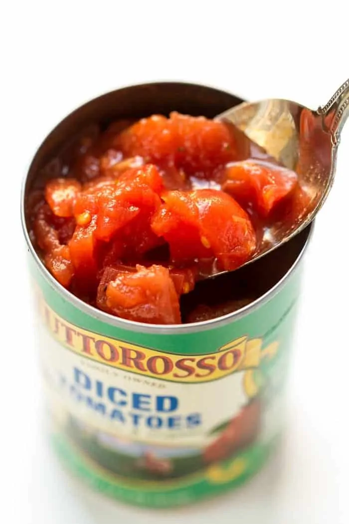 A spoon dipped into an open can of Tuttorosso diced tomatoes.