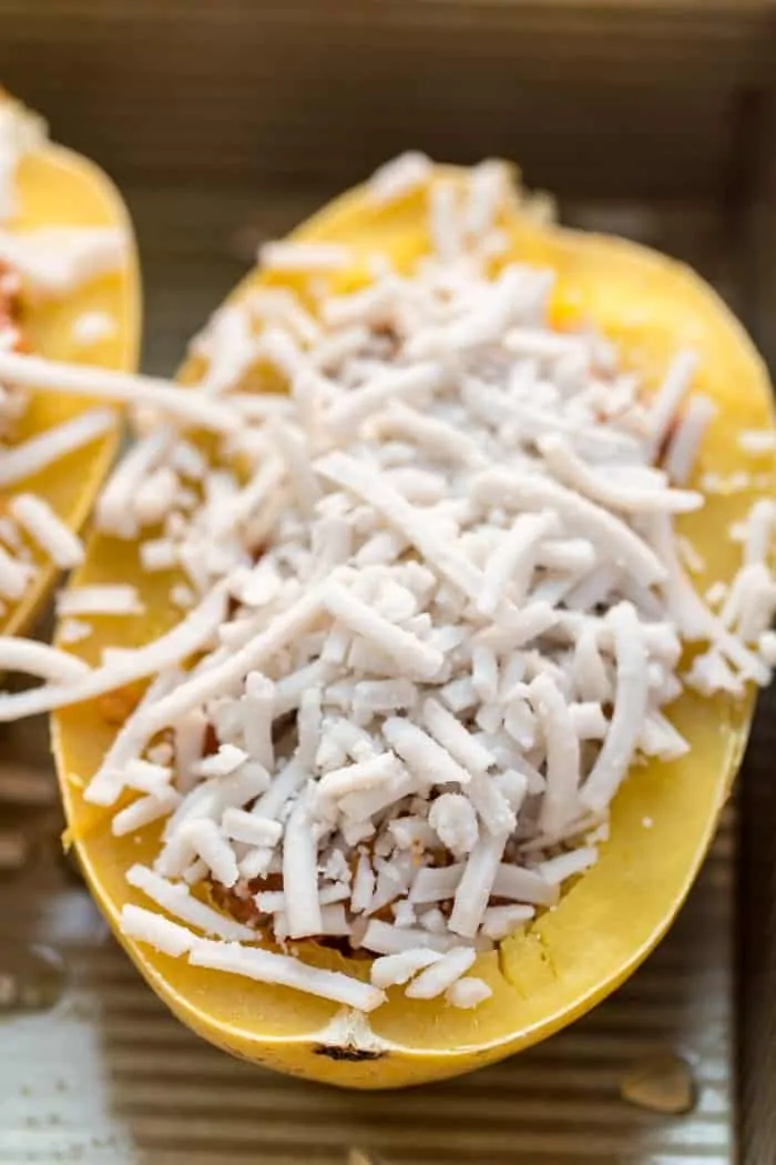 An unbaked spaghetti squash boat filled with vegan bolognese sauce and topped with shredded vegan cheese.