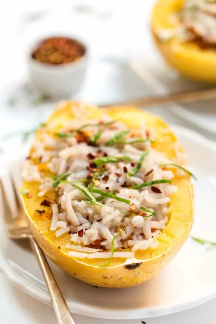 A cheesy spaghetti squash boat on a white plate next to a fork.