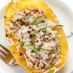 Overhead view of a cheesy spaghetti squash boat on a white plate next to a fork.