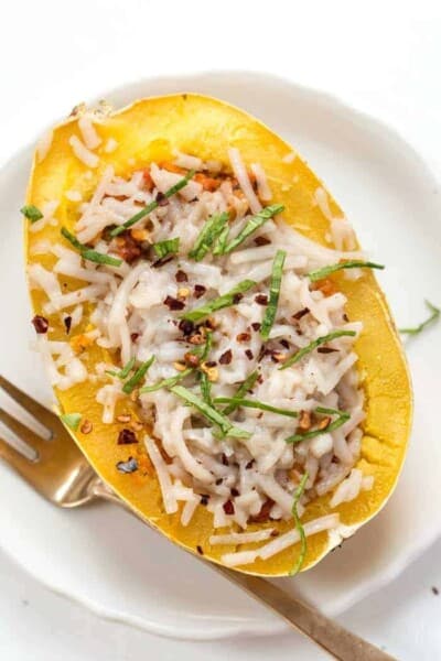 Overhead view of a cheesy spaghetti squash boat on a white plate next to a fork.
