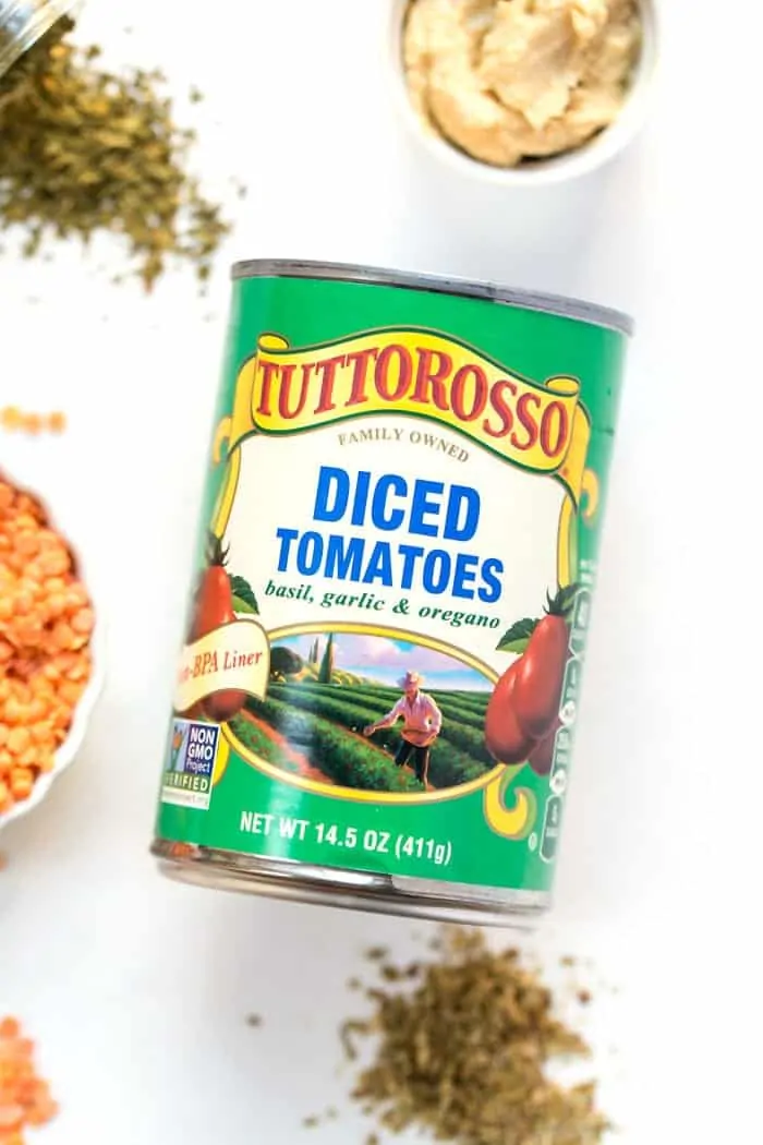 A can of Tuttorosso diced tomatoes on a countertop next to herbs and spices.