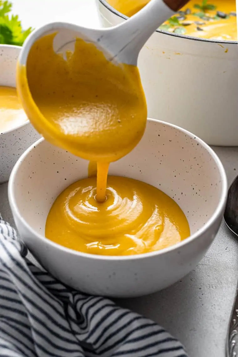 pouring cauliflower and acorn squash soup into a bowl with a ladle