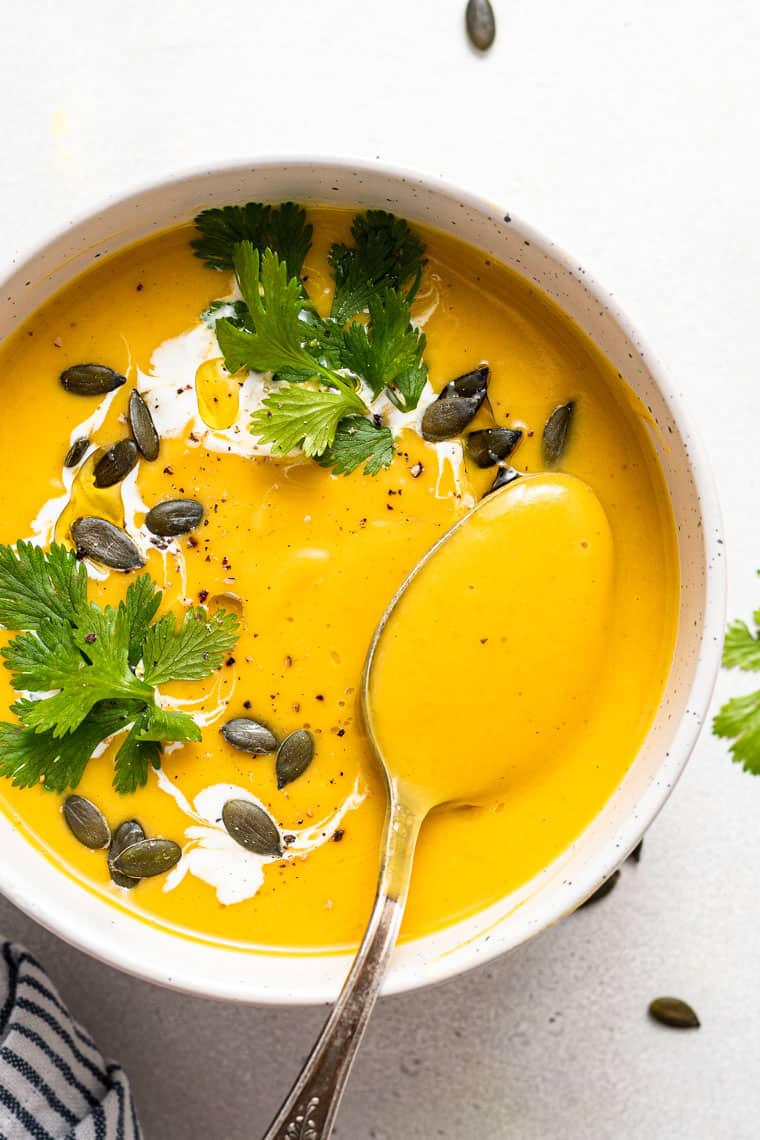 This curried acorn squash soup recipe is cozy and creamy, packed with roasted cauliflower, veggies, and spices. Vegan and freezer-friendly! white bowl of curried acorn squash soup with pumpkin seeds