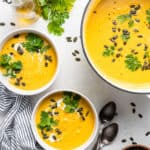 bowls and pot of curried acorn squash soup with pumpkin seeds