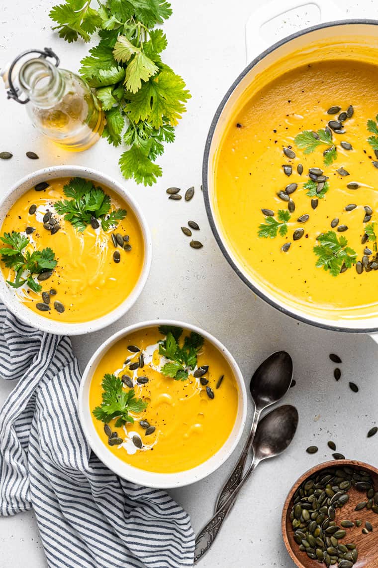 This curried acorn squash soup recipe is cozy and creamy, packed with roasted cauliflower, veggies, and spices. Vegan and freezer-friendly! bowls and pot of curried acorn squash soup with pumpkin seeds